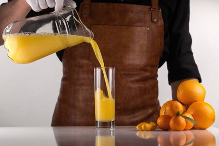 Chef pouring orange juice into a glass on a white surface.の写真素材