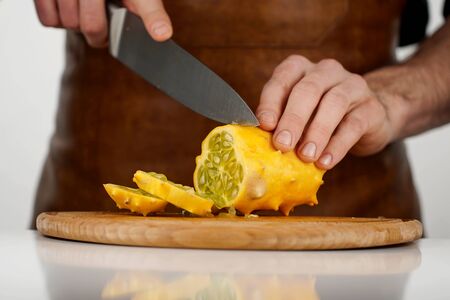 Man cutting tropical fruit kiwano into slices on a wooden cutting board on white backgroundの写真素材