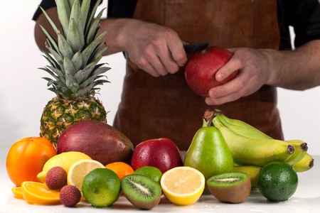 COmposition of ripe fresh tropical fruits on a white table. Man peleeng pomegranate with the help of knifeの写真素材