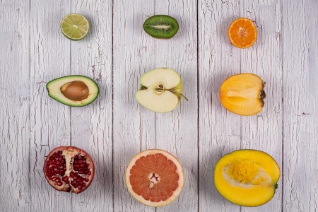 Halves of different tropical fruits placed on a white wooden board in rowsの写真素材