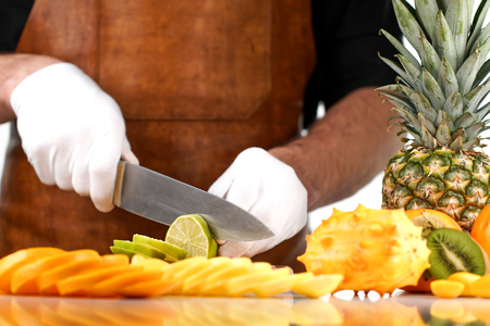 Chef slicing lime on a wooden cutting board among other tropical fruitsの写真素材