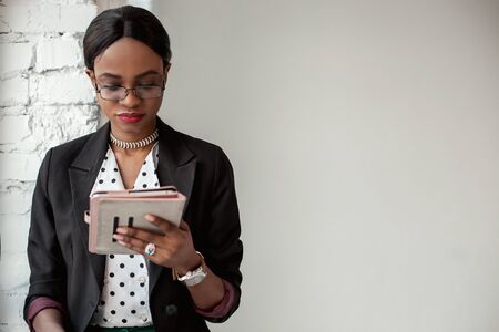 Business woman holding the tablet and wearing glasses. Woman sitting near the window. Official style.の写真素材