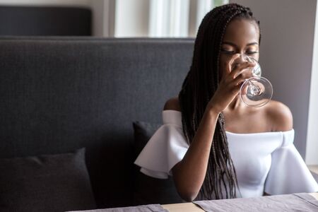 African american girl sitting in a cafe or a restaurant and drinking wine.の写真素材