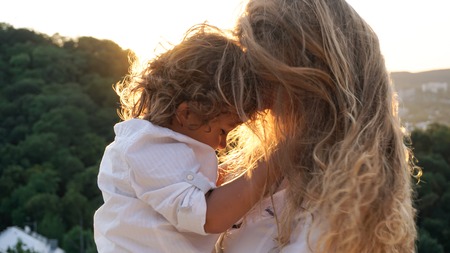 Pretty blonde woman holding her little son. Mother and son standing face to face.の写真素材