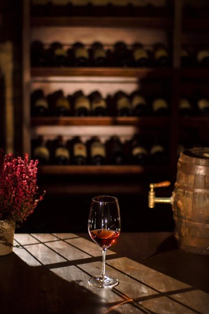 Wine glass placed next to the wine barrel and flower pot on a wooden table in a wine vault.の写真素材