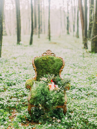 The vertical photo of the moss chair and bouquet placed on it surrounded by trees in the green forestの写真素材