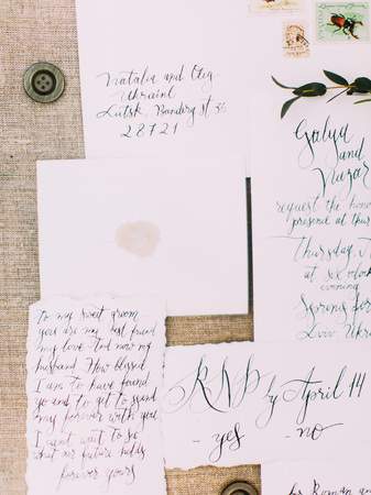 The lovely composition of letters, invitations and postcards writen in beautiful calligraphy and placed on the rustic tissue decorated with buttonsの写真素材