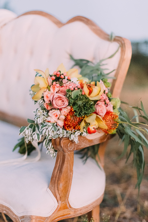 The colourful bouquet consisted of the pink and yellow roses are placed on the wooden knob of the white stylish sofaの写真素材