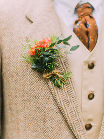 The close-up photo of the red mini-bouquet pinned with the rope on the vintage coatの写真素材