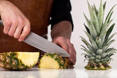 Man cutting pineapple into pieces on a white surface