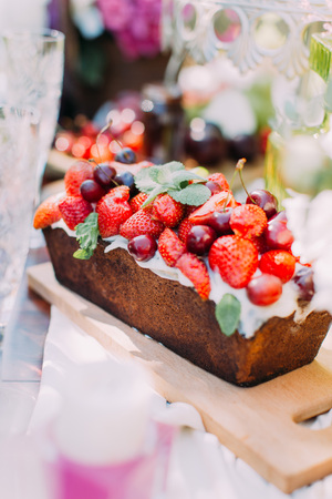 The close-up portrait of the delicious cake derorated with the strawberries and cherries located on the wooden boardの写真素材