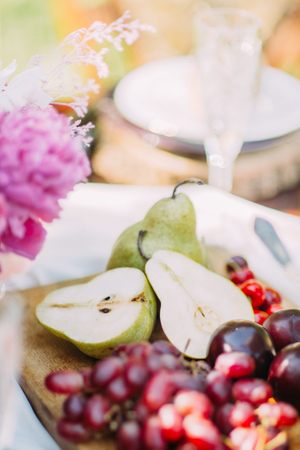 The close-up portrait of green pears located on the wooden board near the dark grapes at the blurred backgroundの写真素材