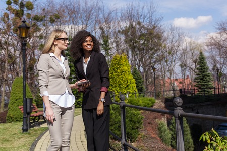 One black and one white businesswomen walking in the park and having conversation.の写真素材
