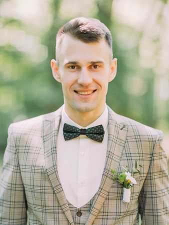 The vertical portrait of the smiling groom at the background of the park.の写真素材