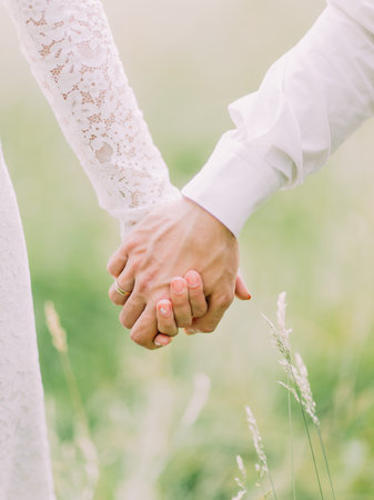 The holding hands of the newlyweds at the background of the sping field. Close-up.の写真素材