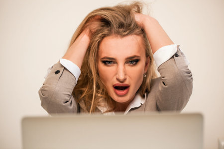 Emotional businesswoman sitting in front of her laptop with her hands by her head. Attractive blonde...