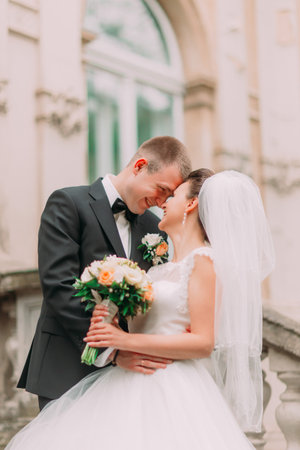 The sensitive side portrait of the smiling newlyweds standing head-to-head.
