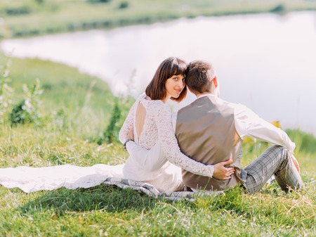 The back view of the newlyweds sitting on the grass and enjoying nature.の写真素材
