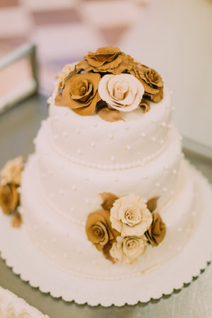 The close-up view of the white wedding cake decorated with chocolade roses.