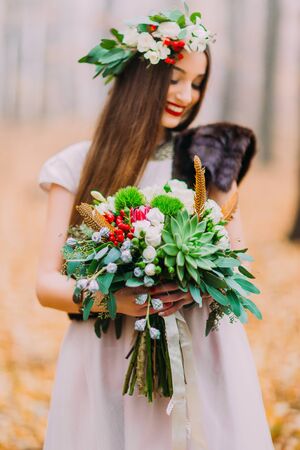 Wonderful bride with wedding bouguet happily smiling. Autumn forest on backgroundの写真素材