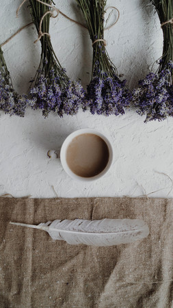 Close-up view of the cup of coffee surrounded by little bouquets of dry lavender and feather. Vintage composition.の写真素材
