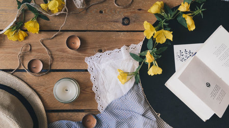 Romantic composition consisting of aroma candles, yellow flowers, book and postcard on the wooden...