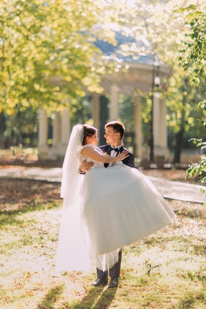 The groom is holding the bride in the long white dress in the park.の写真素材
