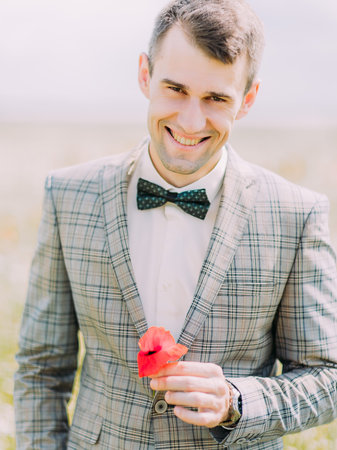 The close-up portrait of the smiling groom holding the poppy.