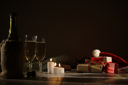 Christmas composition of the wrapped presents, glasses of champagne,wine bottle and glowing candles in the dark roomの写真素材