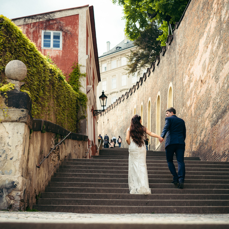The magnificent newlyweds are going up the old baroque stairs. Prague location. The close-up back view.の写真素材