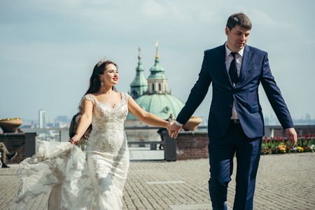 Close-up horizontal view of the cheerful newlywed couple holding hands and walking along the streets of Prague.の写真素材