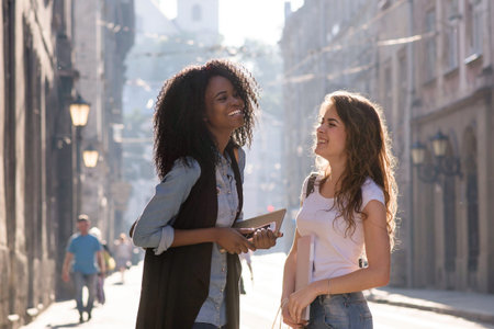 Smiled friends having conversation on the street. One girl is black with long curly hair.の写真素材