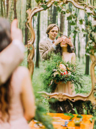The newlyweds in the vintage clothes and the reflection in the mirror. The groom closes the bride`s eyes.の写真素材