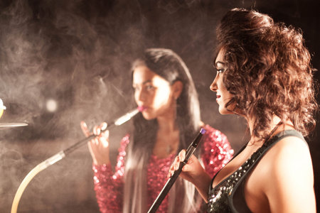 Young, beautiful women smoke a hookah in cafe. It produces smoke from their mouthes. The pleasure of...