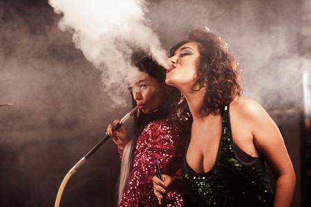 Sexy girls exhaling hookah smoke from their mouthes. Women with bright makeup and nice hairstyles.の写真素材