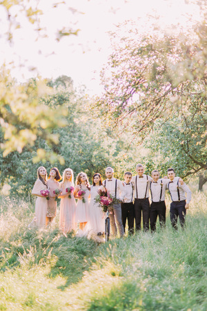 The full-hight photos of the newlywed couple, best men and bridesmaids holding the bouquets of the pink flowers in the forest.の写真素材