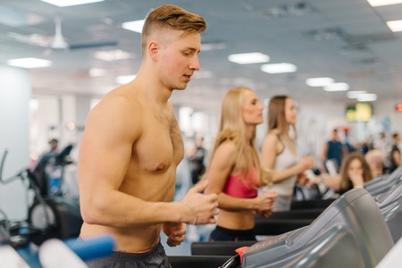 Young man running on treadmills in gym. Guy with bare body looking at the displayの写真素材