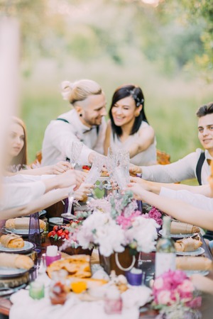 The close-up photo of the table setting and the glasses at the background of the blurred newlyweds and guests clinking the glasses in the forest.の写真素材