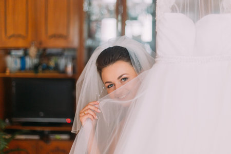 Beautiful bride hiding her face with a light veil of wedding dress