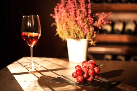 Wine glass placed nex to the bunch of grapes and flower pot. Wooden table on a wine vault.の写真素材