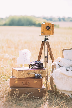 The vertical photo of the part of the sofa placed next to the vintage suitcases, old camera and typewriter at the background of the sunny spring.の写真素材