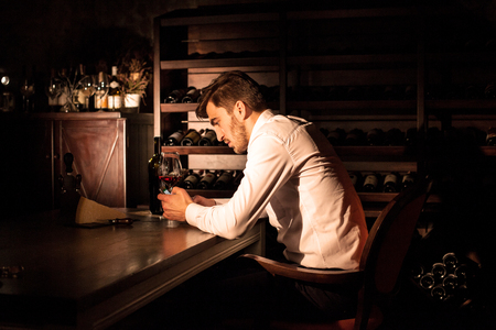 Man in a white shirt sitting by the table with the phone in his hands.の写真素材