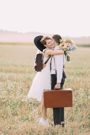 The lovely side portrait of the happy vintage dress newlyweds hugging in the sunny field.の写真素材