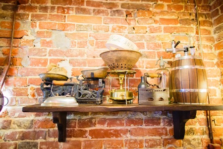 The front view of the vintage composition consisted of the barrel, irons, antique weight and bottles place on the wooden shelf in the front of the brick wall of the cafeの写真素材
