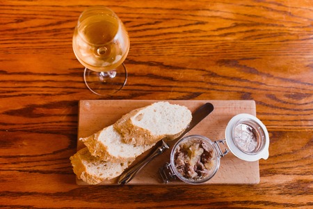 The horizontal above view of the food composition consisted of the bread and jar of meat on the wooden board standing near the glass with white wineの写真素材