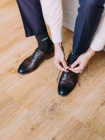 Close-up view of the hands of the groom buttoning his wedding shoesの写真素材