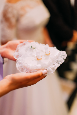 The bride is holding the pillow in the form of the heart with wedding rings on itの写真素材