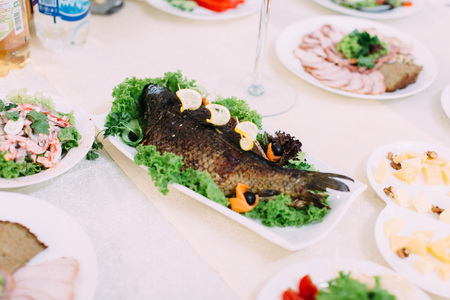 The baked fish with lemons decorated with different vegetables. The wedding table setの写真素材