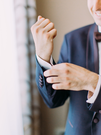 Close-up view of the hand of the groom buttoning the wedding jacketの写真素材