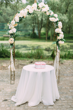 Lovely decorated arch with white flowers behind the table with tiny pink box on itの写真素材